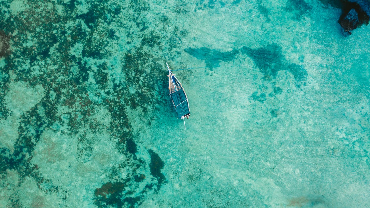 Drone shot of a boat floating in clear turquoise waters of Zanzibar, Tanzania. Serene and scenic top view.